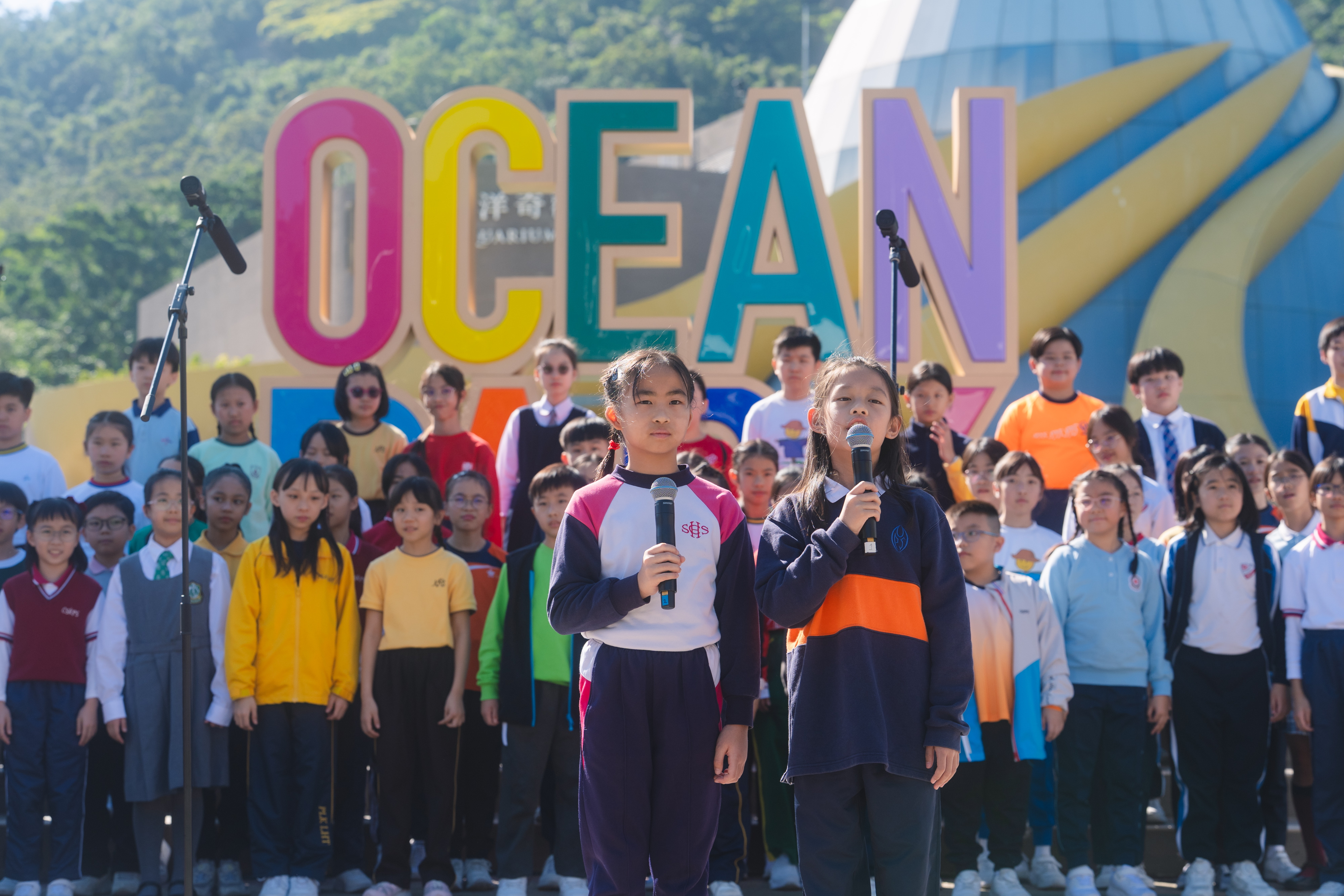 Two young singers holding microphones before a large audience at an HKVC programme