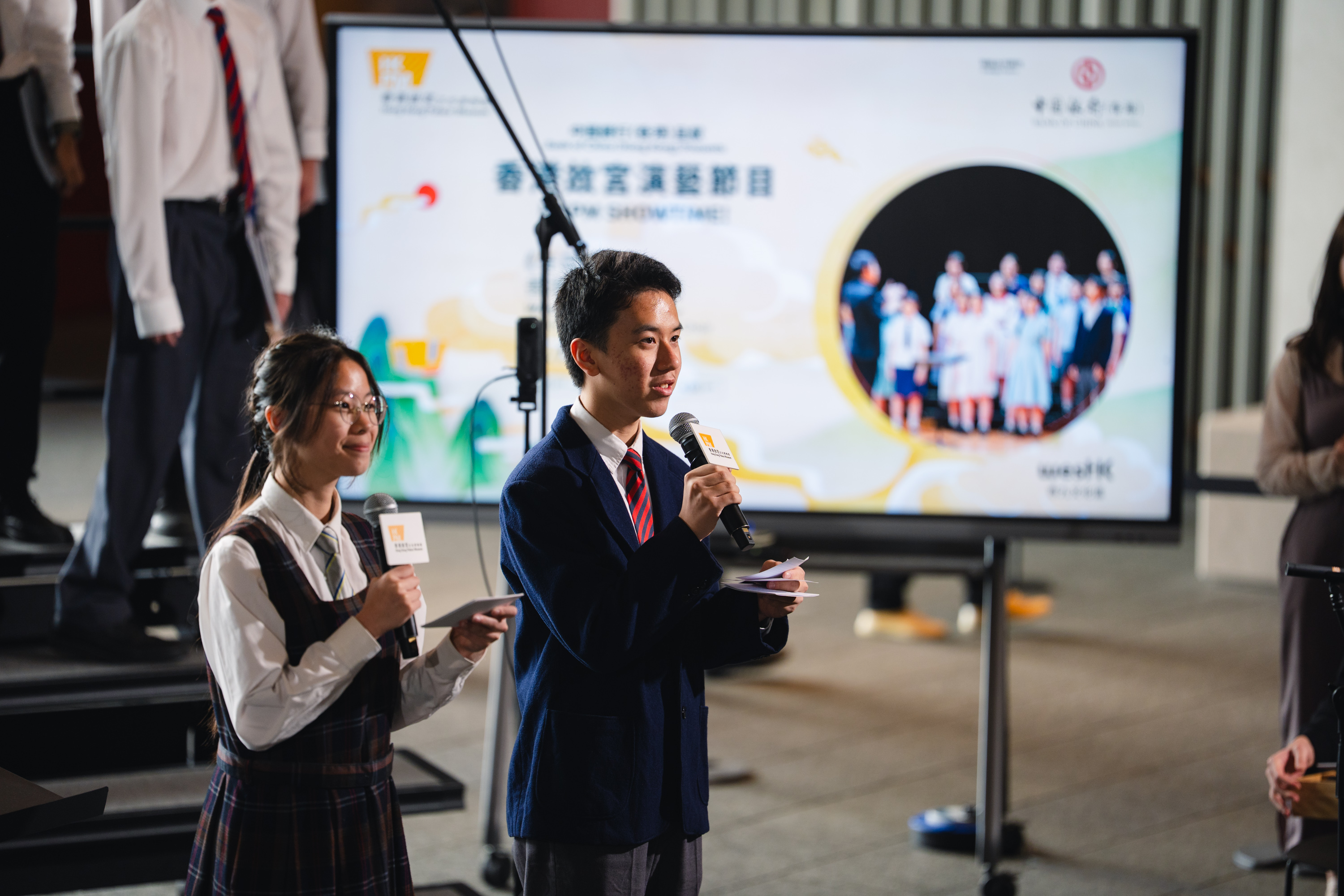 Two student hosts presenting with microphones at an HKVC event