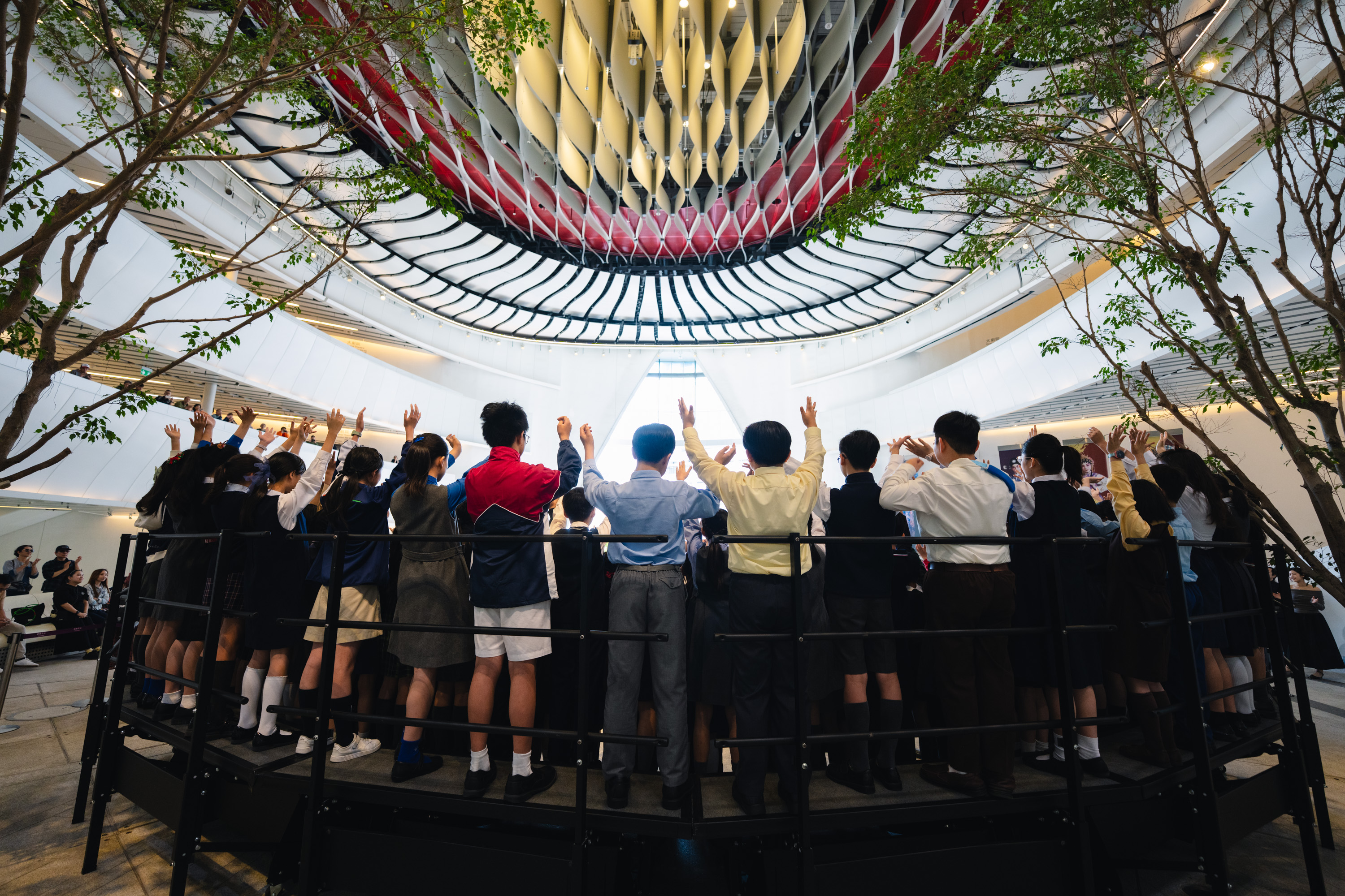 A school choir with arms raised performing in a bright atrium at an HKVC programme in December 2025