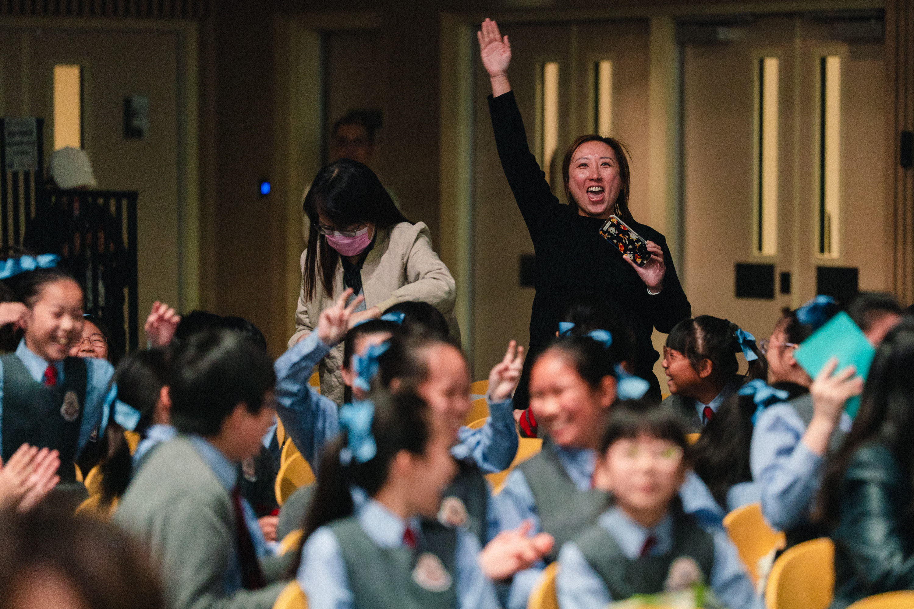 Teacher cheering with a raised hand among excited school students