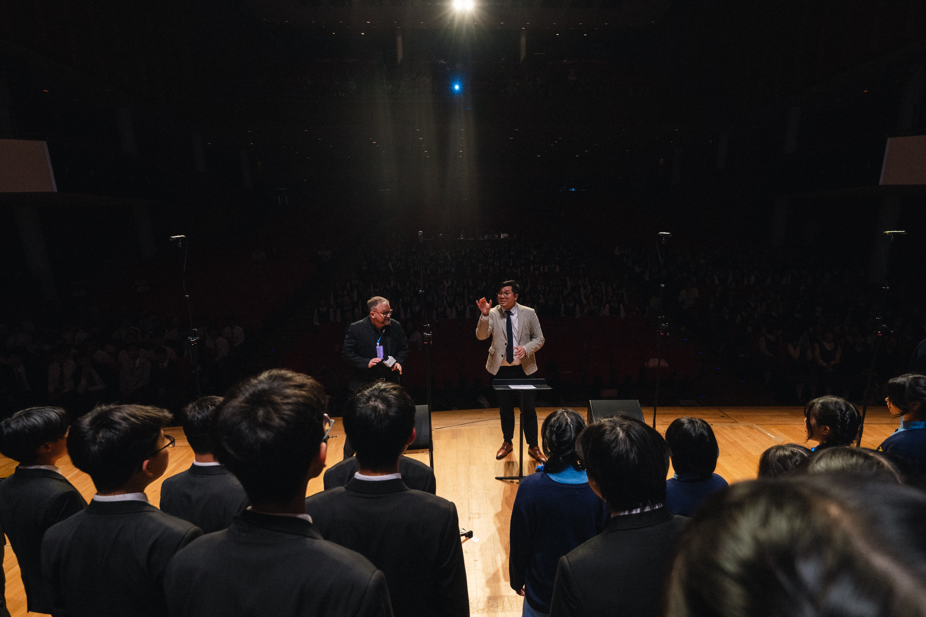 A conductor coaches a school choir from the stage at an HKVC festival event in Hong Kong