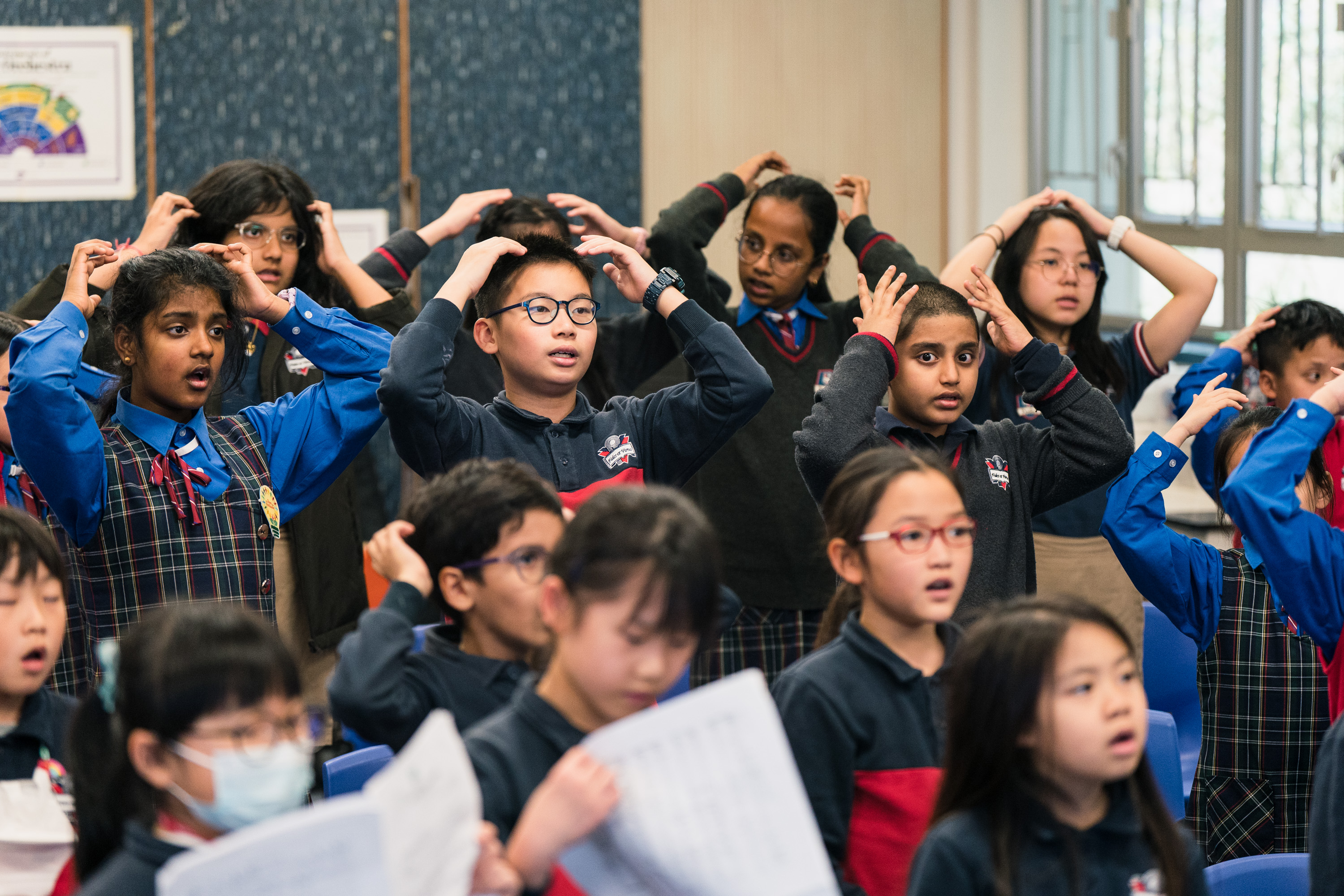Primary school students singing with their hands on their heads during an HKVC classroom choral activity